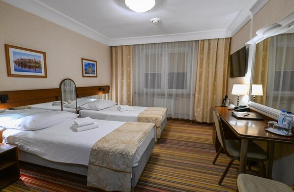 A hotel room with two beds, a desk, a chair, a mirror, and two framed pictures on the wall.