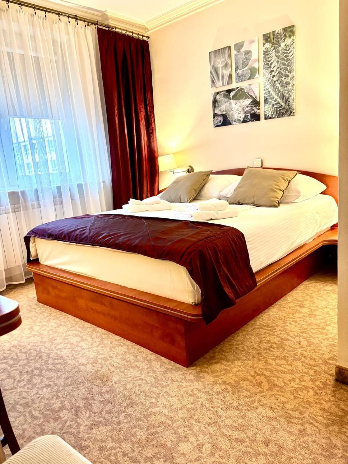 A hotel room with a large bed, a wooden headboard, a carpeted floor, and a window with curtains.