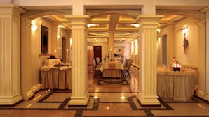Un vestíbulo de hotel con una imponente escalera, columnas y una zona de recepción.
