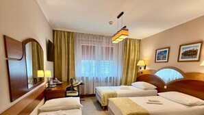 Habitación de hotel con dos camas individuales, un escritorio con silla, un espejo grande, una ventana con cortinas y una lámpara colgante.