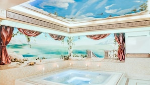 Un baño lujoso con una bañera grande, un mural en el techo y vista al mar.