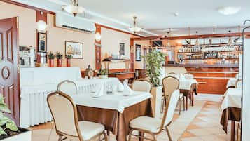 A restaurant with tables and chairs, a bar area with bottles, and a coffee machine.