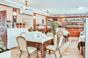 Um restaurante com mesas e cadeiras, área de bar com garrafas e uma máquina de café.