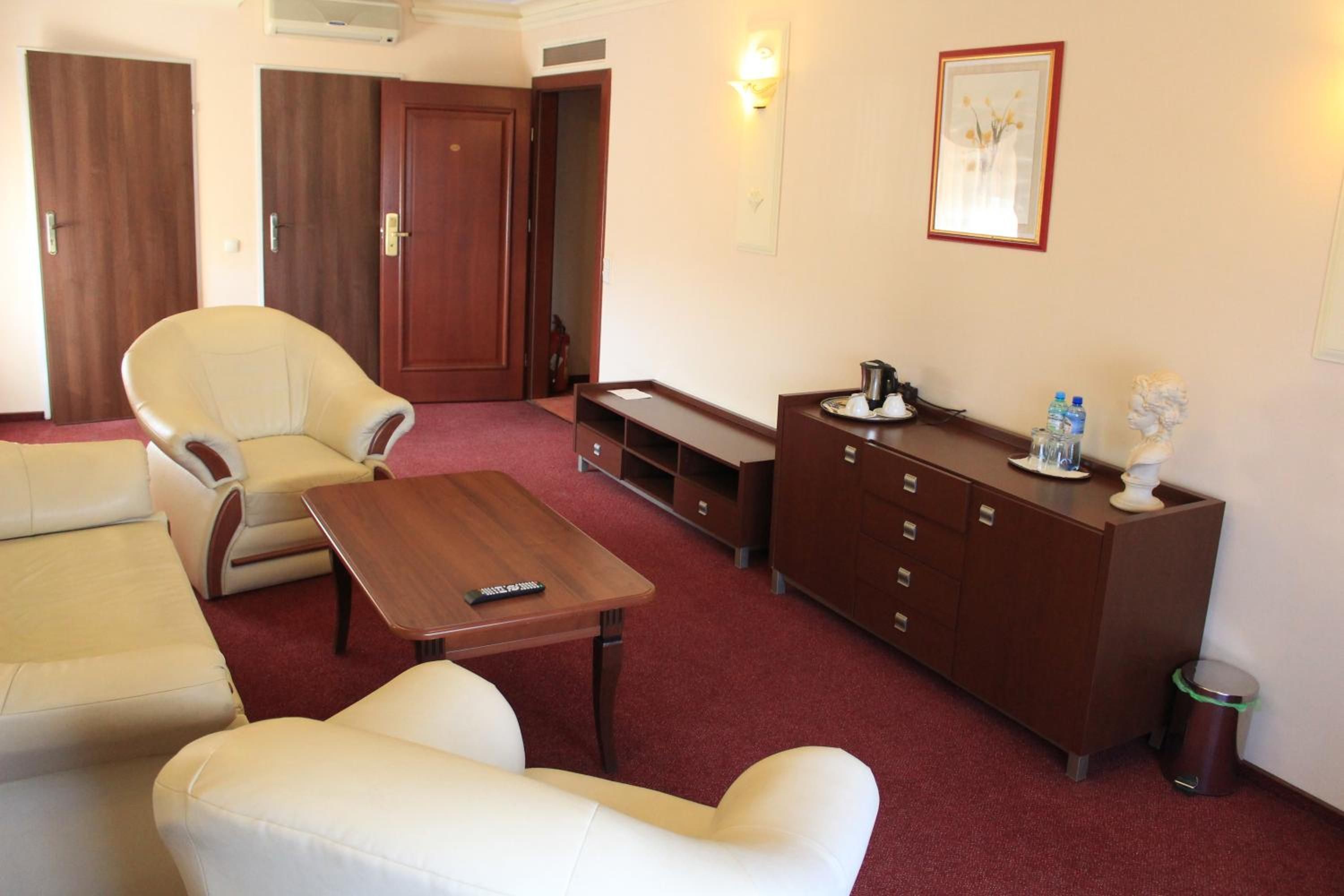 A hotel room with a sofa, armchair, a small table, a cabinet, and a trash bin.