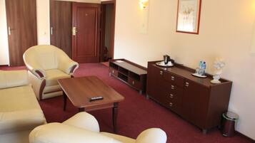 A hotel room with a sofa, armchair, a small table, a cabinet, and a trash bin.