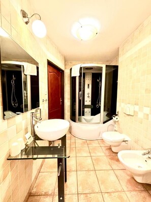 A bathroom with a glass-enclosed shower, a white sink, a toilet, and a bidet.