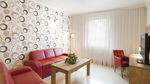 A modern living room with a red sofa, a wooden coffee table, and a red armchair. A decorative wall with circular patterns and a large window with sheer curtains are visible. - Dworek Eureka (Czechowice-Dziedzice)