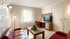 A modern living room with a sofa, a coffee table with a floral arrangement, a television on a wooden stand, and a red chair. - Dworek Eureka (Czechowice-Dziedzice)