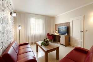 Una sala moderna con un sofá, una mesa de centro con un arreglo floral, un televisor sobre un mueble de madera y una silla roja.