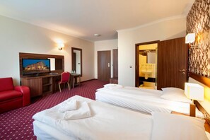A hotel room with two beds, a TV, a desk, a red chair, and a wardrobe.