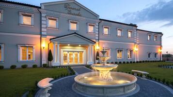 Un hotel grande con una entrada imponente, una fuente y jardines bien cuidados.