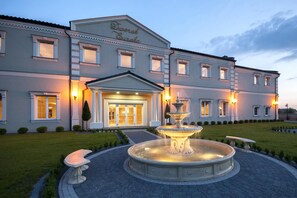 A large hotel with a grand entrance, a fountain, and well-maintained gardens.
