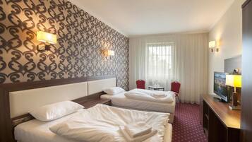 Habitación de hotel con dos camas, televisión, escritorio y ventana con cortinas.