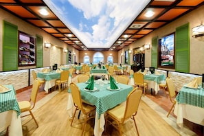 Um restaurante com várias mesas, toalhas de mesa xadrez verdes, cadeiras de vime e um teto com design que lembra o céu.