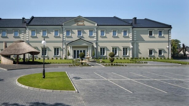 A large, two-story building with a symmetrical facade, a central entrance with a portico, and a parking lot in front. - Dworek Eureka (Czechowice-Dziedzice)