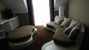 Un espacio habitable moderno y funcional con un sofá curvo y su reposapiés, un televisor de pantalla plana pequeño y una ventana con cortinas.