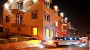 Un hotel de varios pisos con balcones y un coche estacionado adelante.