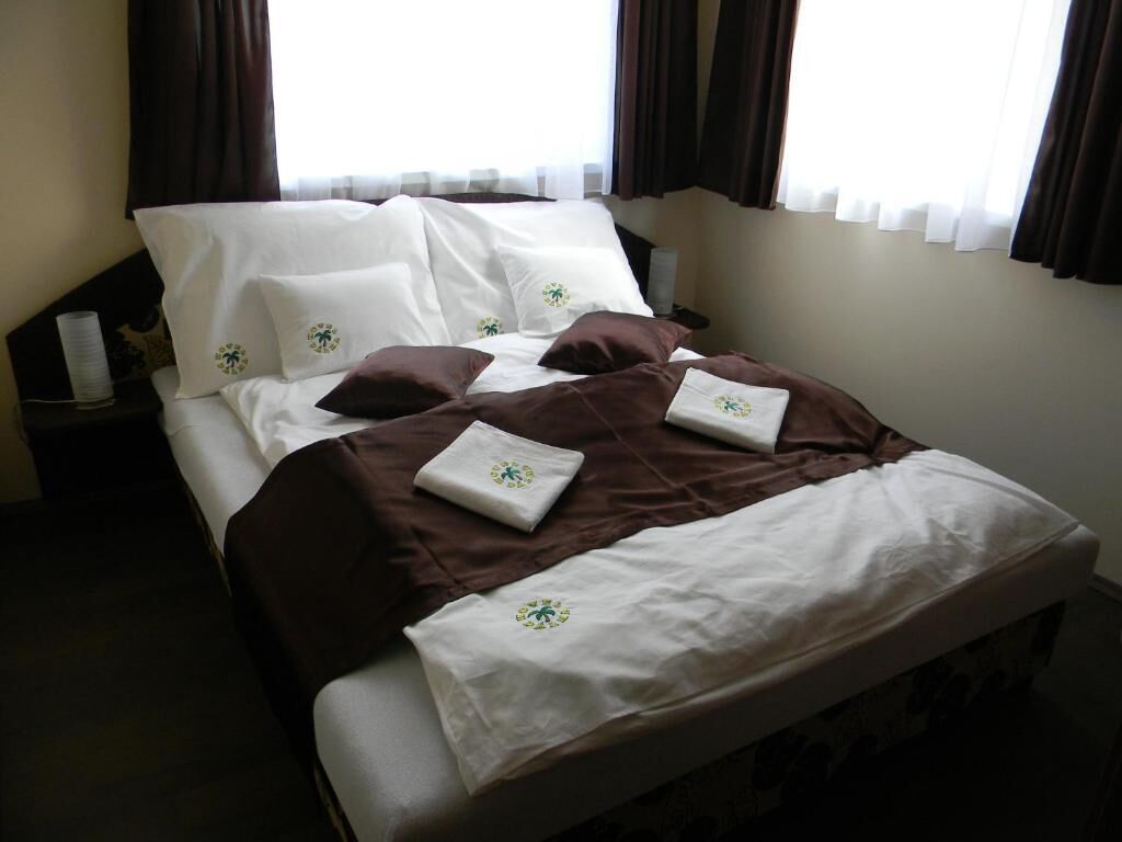 A neatly made bed with white and brown bedding, a small bedside table with a lamp, and a window with curtains.