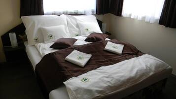 A neatly made bed with white and brown bedding, a small bedside table with a lamp, and a window with curtains.
