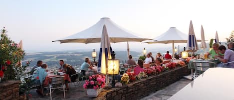An outdoor dining area with tables and chairs, umbrellas, and a view of the landscape.