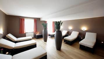A room with multiple seating areas, including sofas and chairs, arranged around large potted plants.