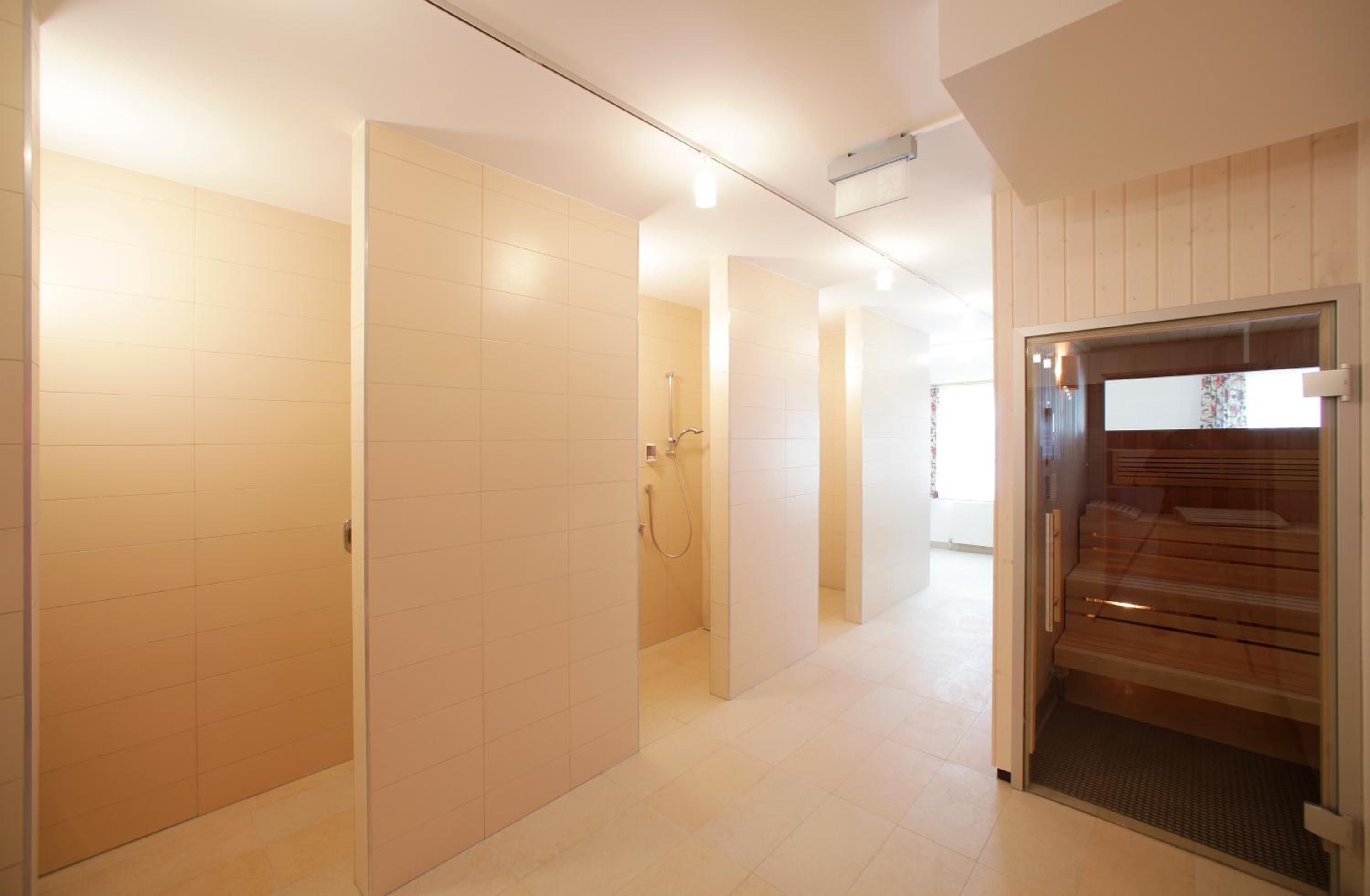 Ein moderner Flur mit weiß gefliesten Wänden und einer Holztür zum Sauna-Bereich.