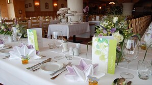 A banquet table set with white tablecloths, silverware, and glassware, with floral centerpieces and name cards.