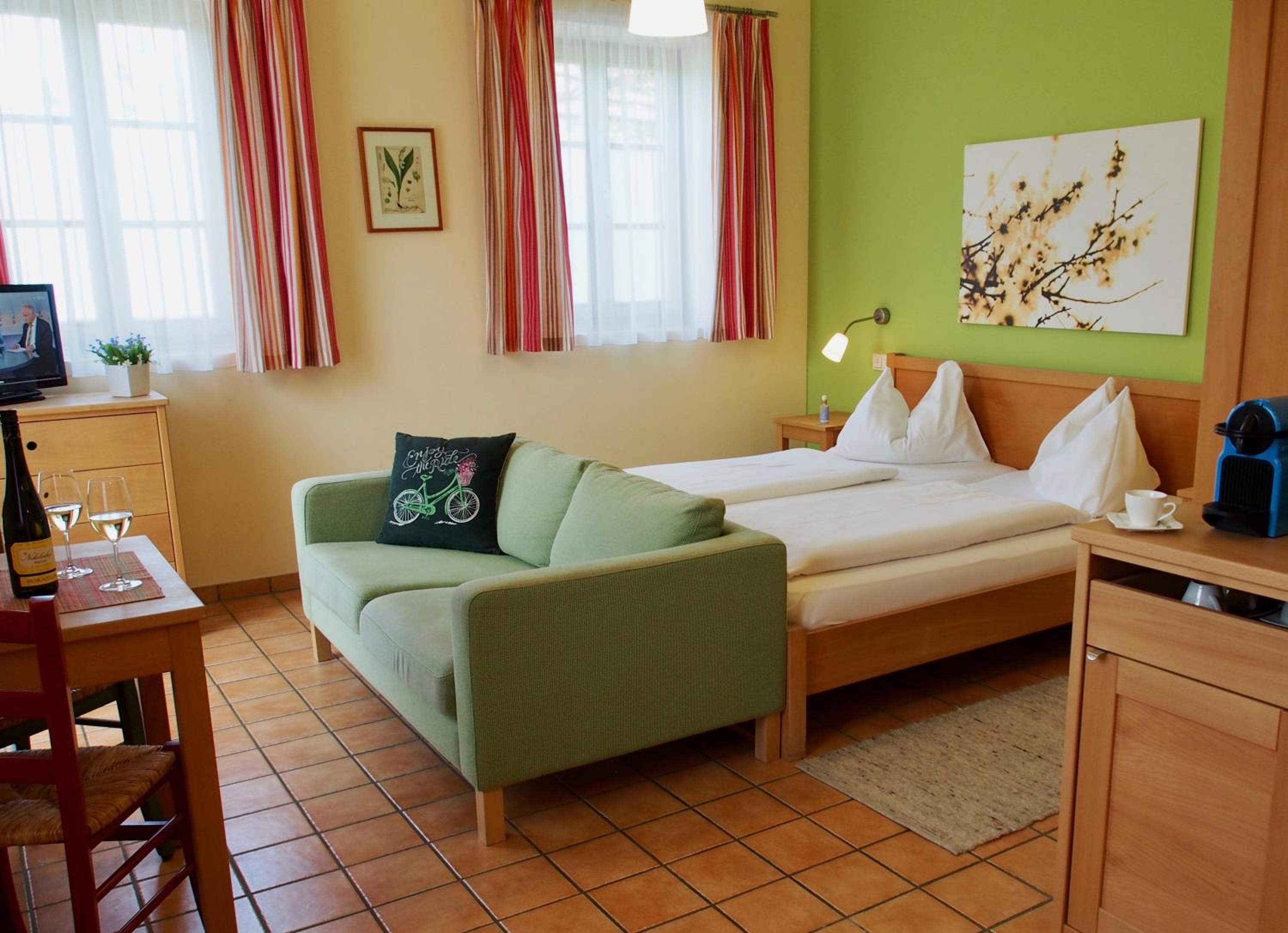 Una habitación de hotel con cama, sofá, escritorio con televisor y ventana con cortinas.