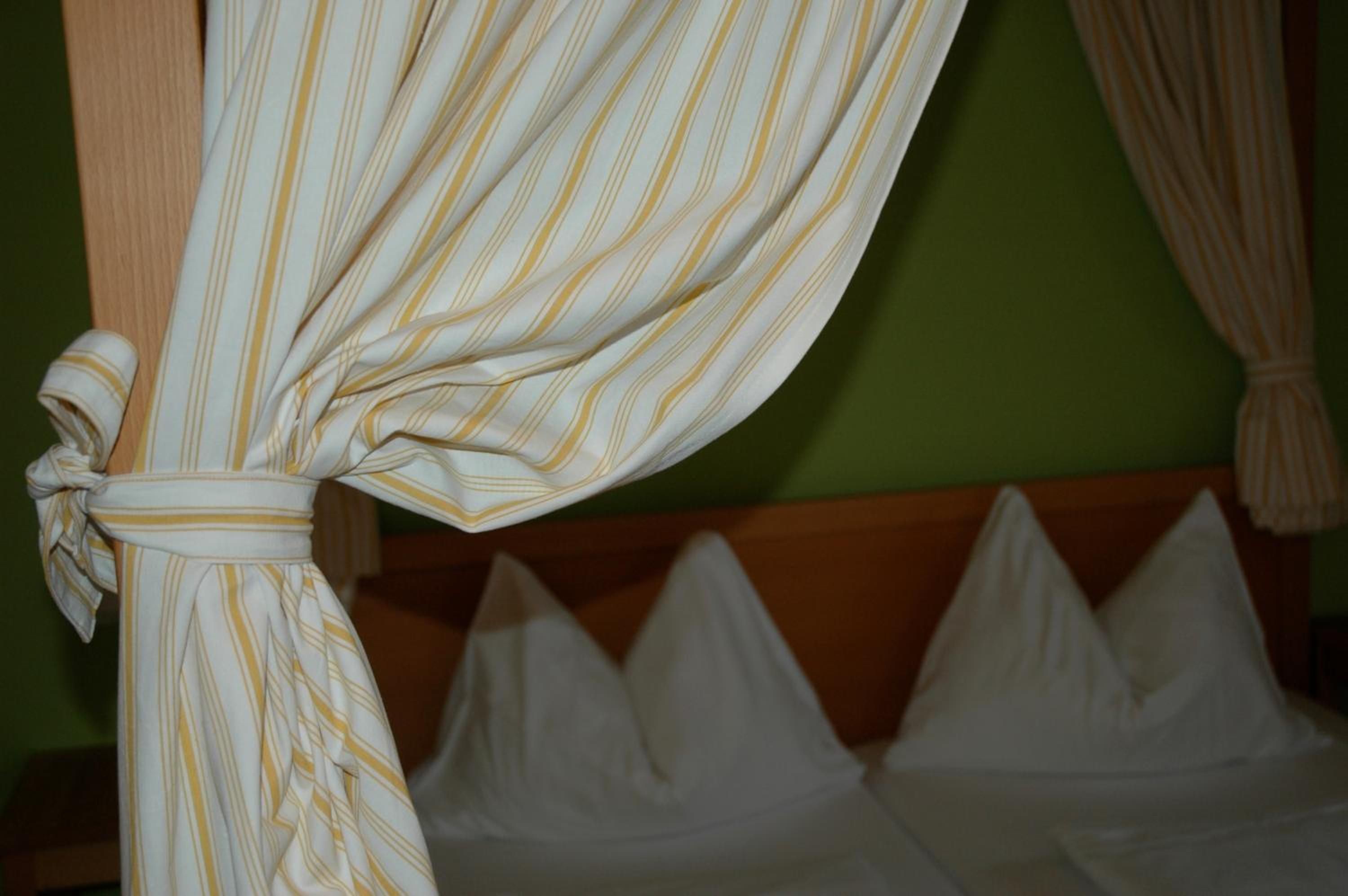 Una cama con almohadas blancas y una cortina a rayas atada al pie de la cama.