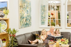 A living room with a leather couch, a bookshelf, a painting, and a window with a view of a garden. - Ad Vineas Gästehaus Nikolaihof-hotel Garni (Mautern an der Donau)