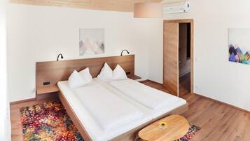 A modern bedroom with a wooden bed, a colorful rug, a small wooden table, and a door leading to another room.