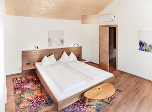 A modern bedroom with a wooden bed, a colorful rug, a small wooden table, and a door leading to another room. - Ad Vineas Gästehaus Nikolaihof-hotel Garni (Mautern an der Donau)