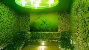 Una habitación con pared de mosaico verde, un candelabro central y un mural de un árbol.