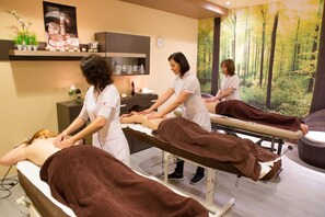 A spa setting with massage tables, a wall with a forest mural, and shelves with products. - Hotel Zawiercie (Zawiercie)