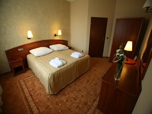 A hotel room with a bed, bedside tables, a wooden dresser, a mirror, and a vase with flowers. - Hotel Zawiercie (Zawiercie)