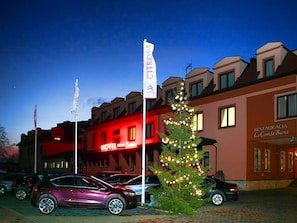 Hotel decorado com árvore de Natal e bandeiras, um letreiro vermelho e carros estacionados.
