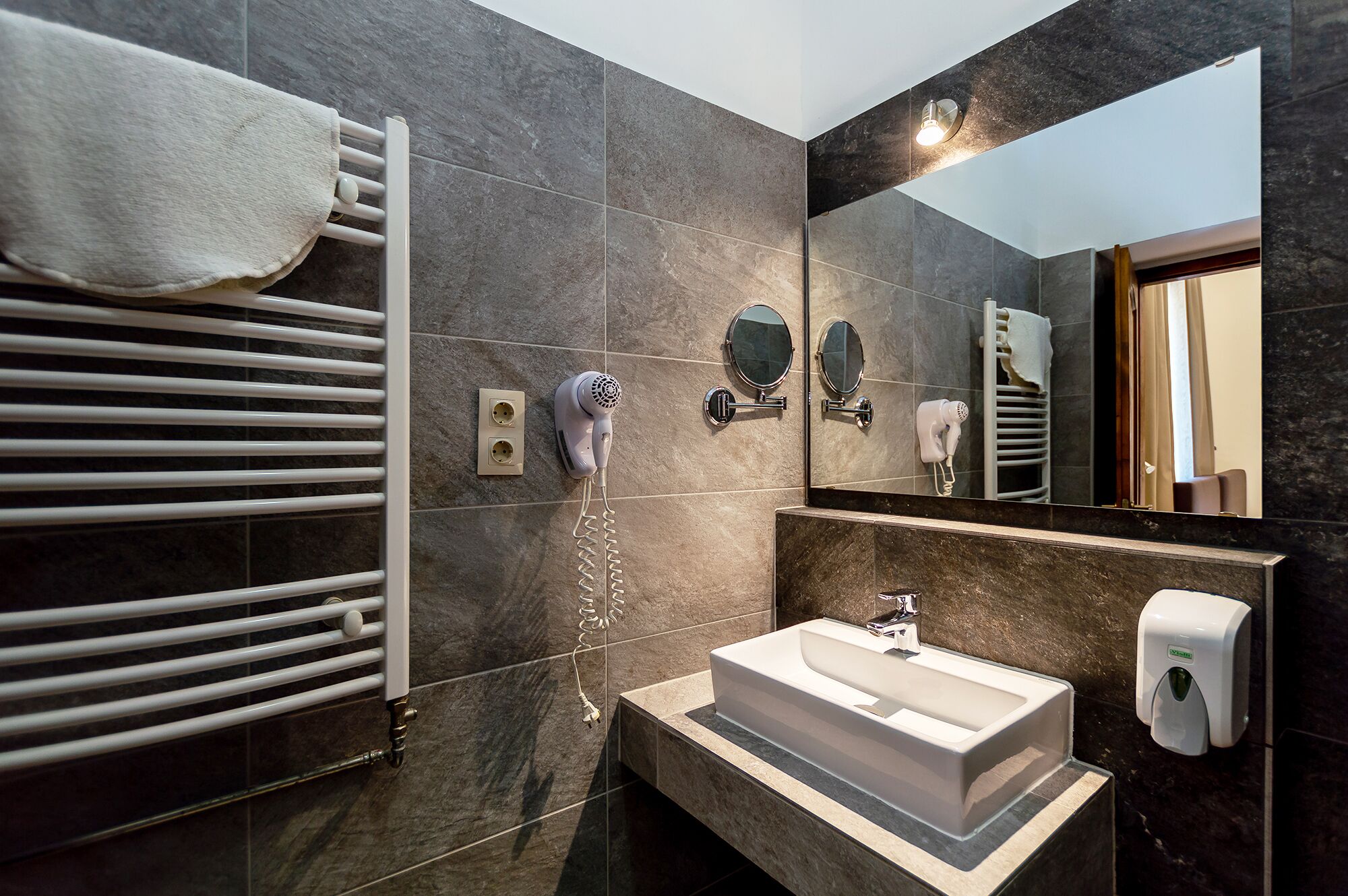Une salle de bain moderne avec un lavabo blanc, un porte-serviettes, un sèche-cheveux et un miroir.