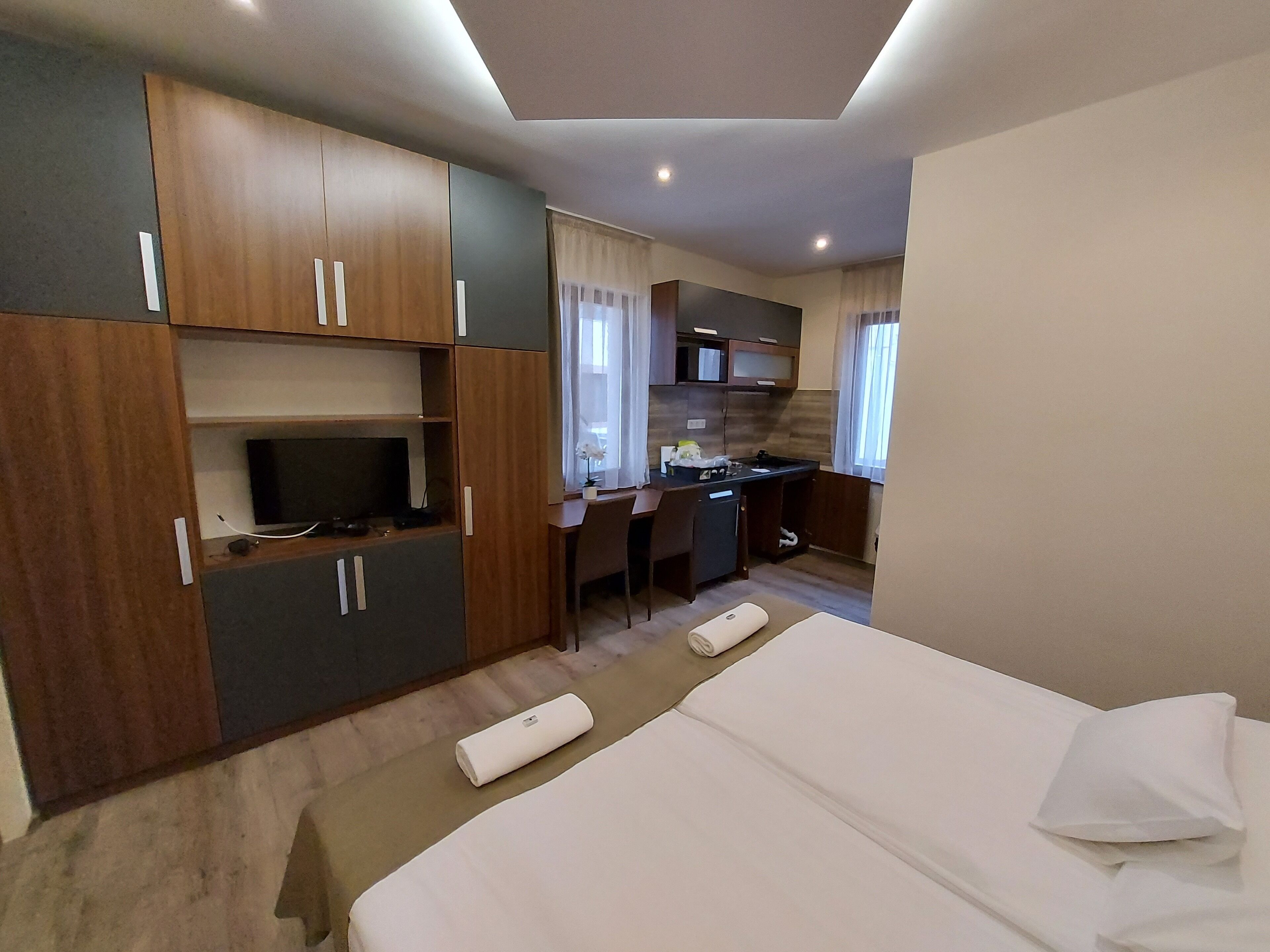 A hotel room with a bed, a desk, a kitchenette, and a TV.