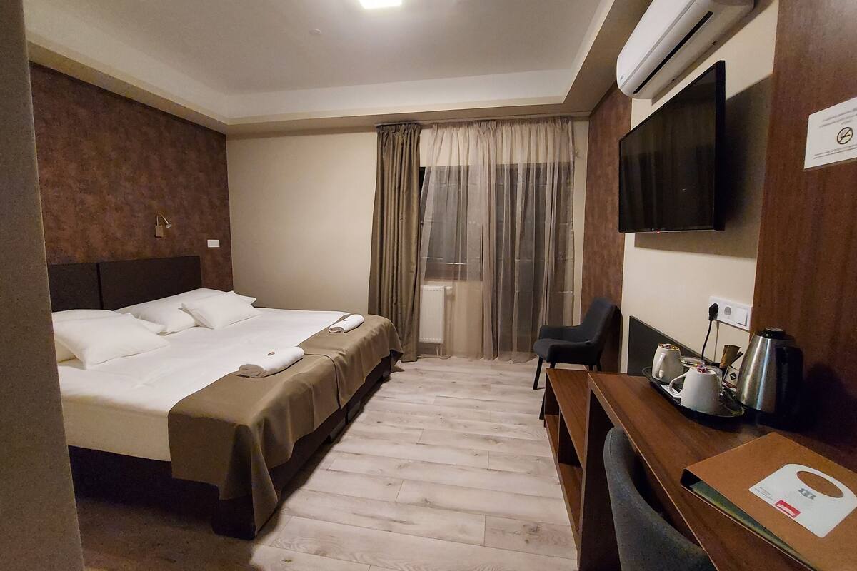 Habitación de hotel con cama, escritorio con silla, televisor y aire acondicionado.