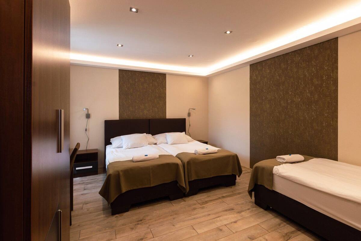 Una habitación de hotel con una cama grande, dos mesitas de noche y una cama más pequeña.