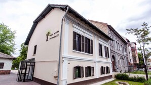 A two-story building with a beige facade, black shutters, and a small garden area in front. - Vén Diófa De Lux Panzió (Szeged)