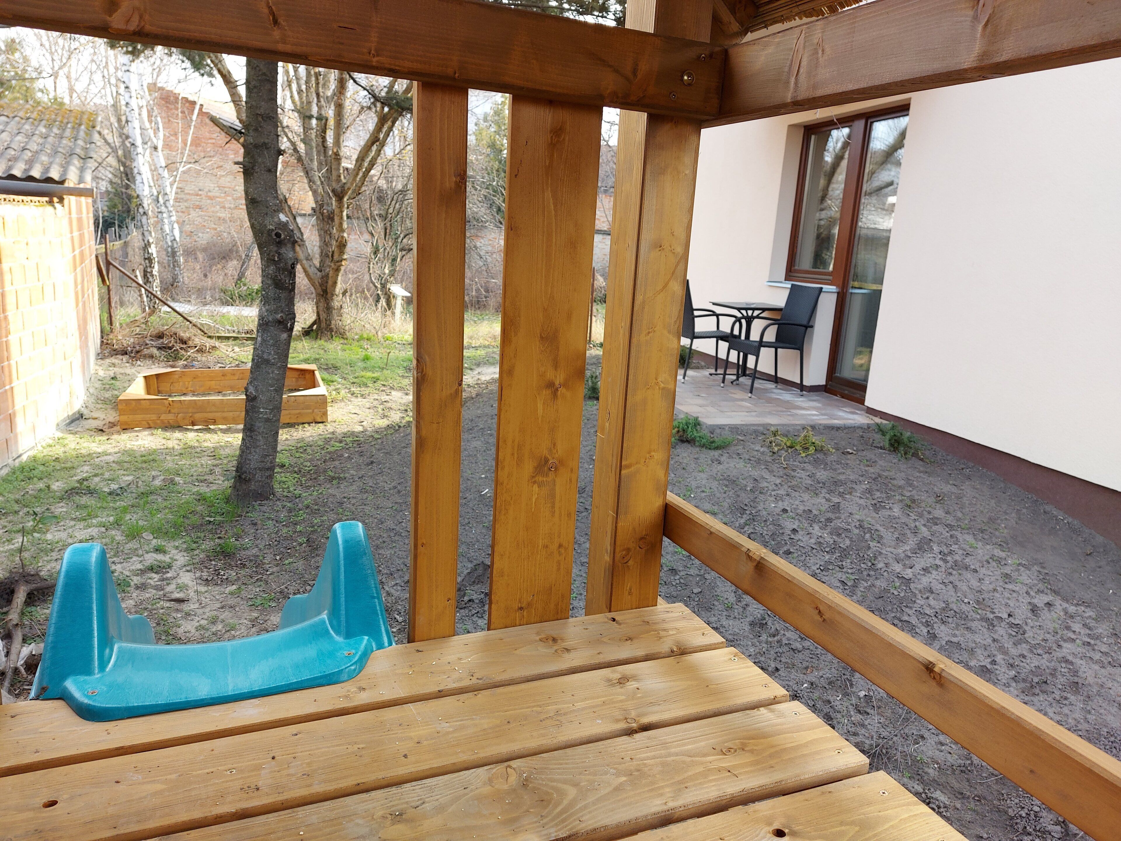 Un pontile in legno con una sedia di plastica blu, una panchina in legno e un tavolo con sedie sullo sfondo.