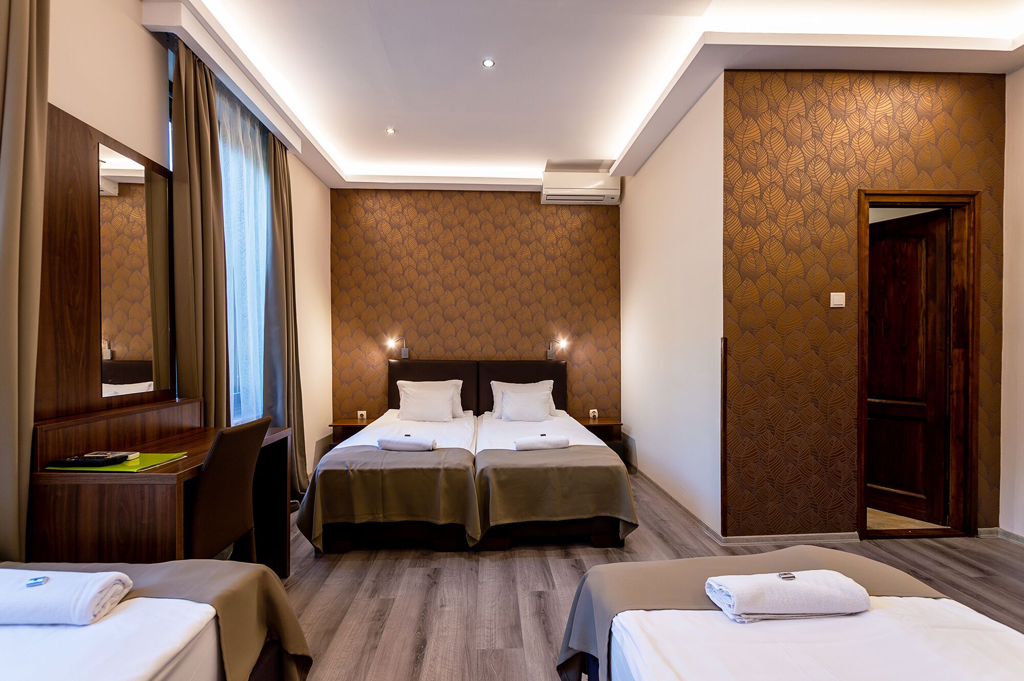 A hotel room with two beds, a desk, a chair, and a large mirror.