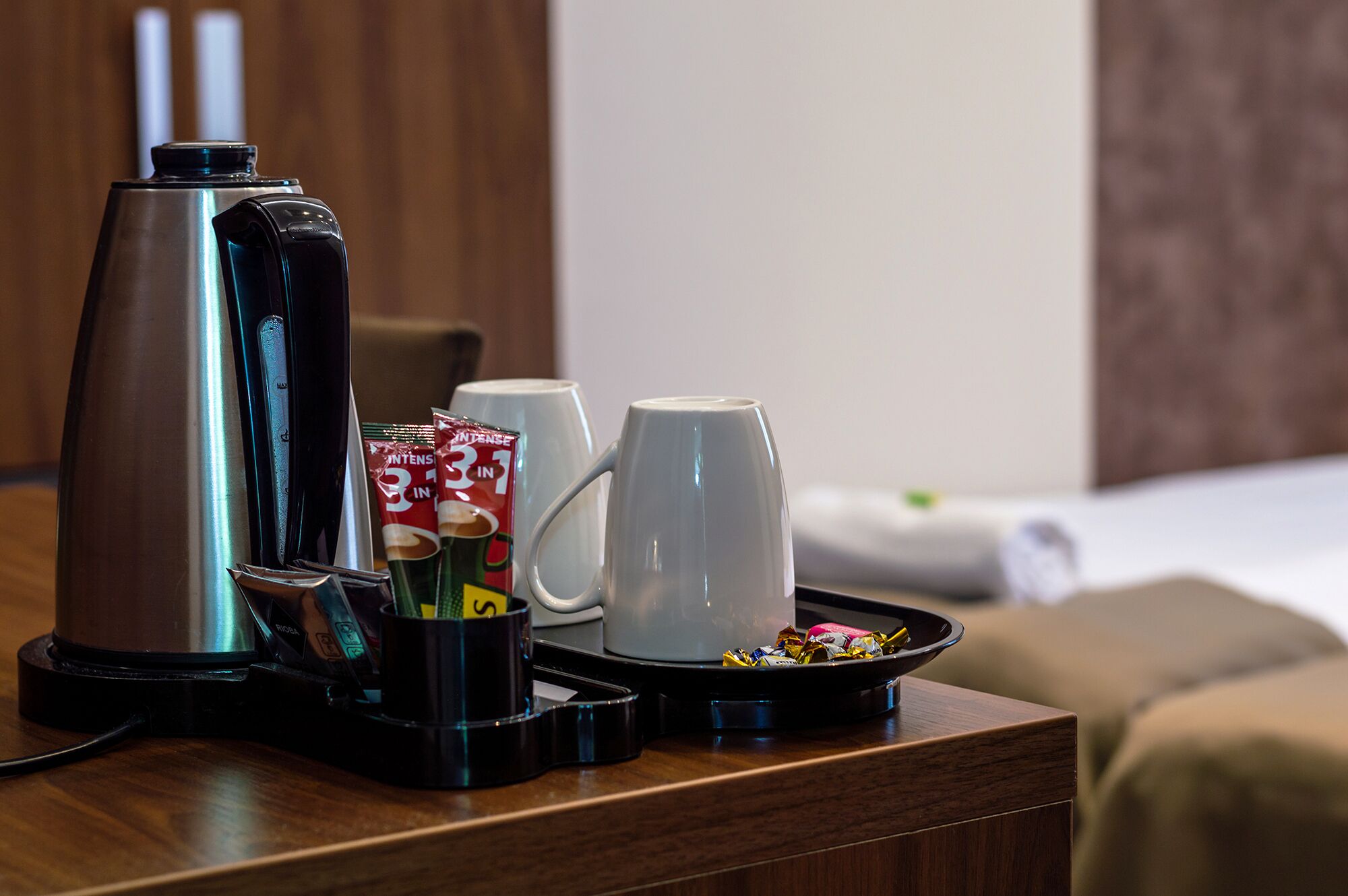 A hotel room with a coffee maker, two cups, and a tray with coffee packets on a wooden table.