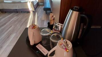Une chambre d’hôtel avec un lit, un banc, un plateau avec des tasses, des pots et une bouilloire.