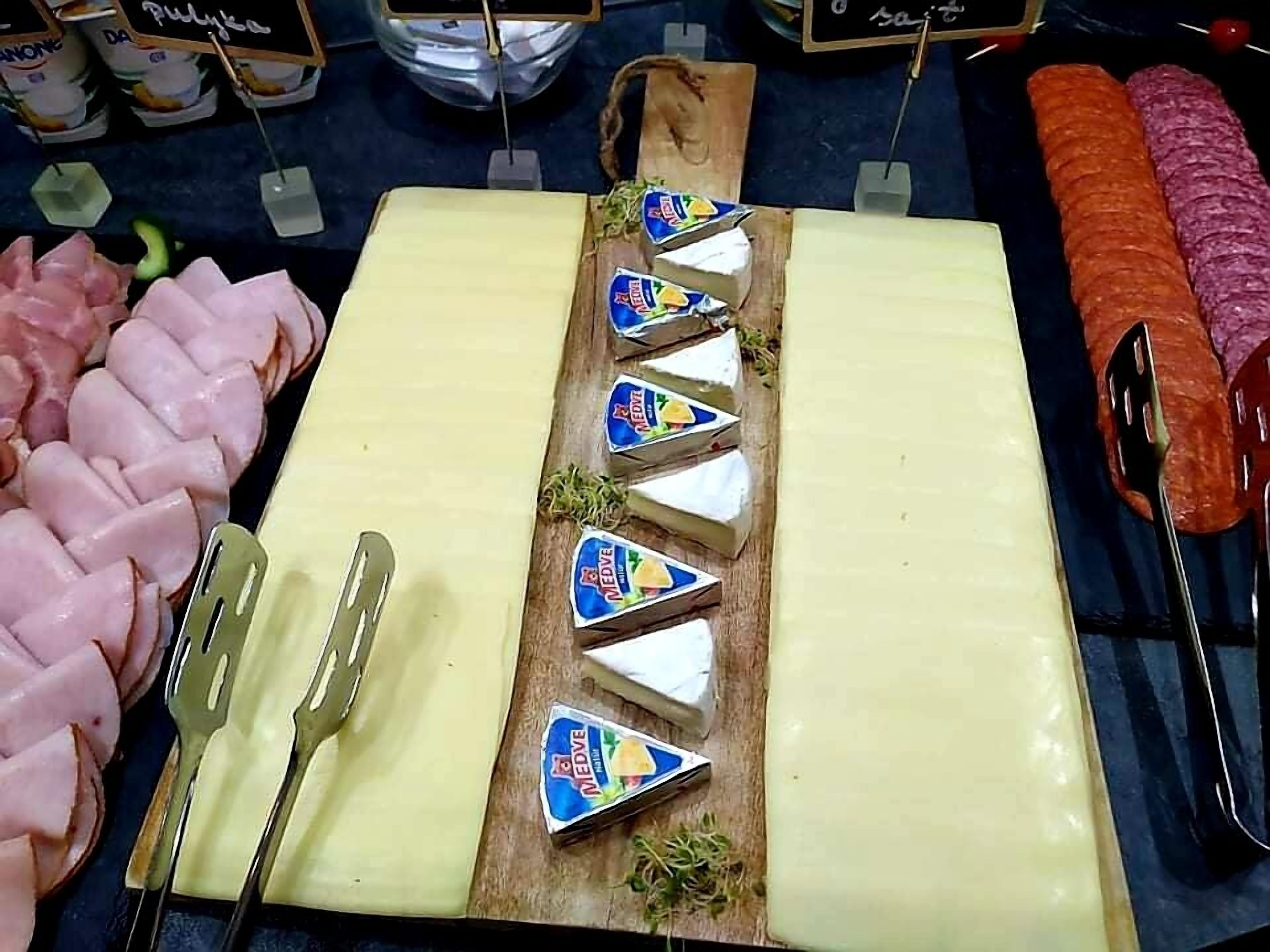 Una tabla de quesos con diversas variedades, un plato de jamón y un salchichón grande sobre una tabla de madera.