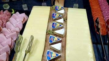 Una tabla de quesos con diversas variedades, un plato de jamón y un salchichón grande sobre una tabla de madera.