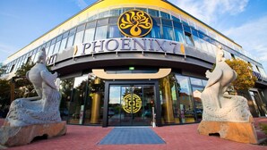 Un edificio moderno con fachada curva, donde se destaca el nombre 'PHOENIX7', y dos grandes estatuas a ambos lados de la entrada.