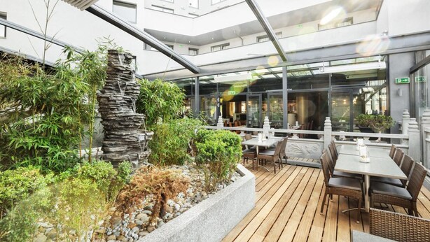 Un área de comedor al aire libre con mesas y sillas, rodeada de vegetación y una formación rocosa.