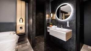 Un baño moderno con tocador, espejo y una cama en la habitación contigua.